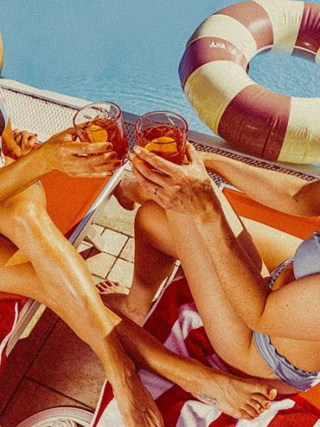 Two people relaxing by the water and toasting with spritz cocktails on sun loungers.